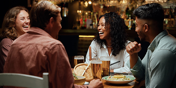 Group of four people laughing and enjoying a pre-show dinner at a restaurant.