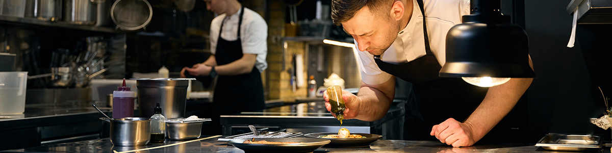 A professional chef plating a gourmet dish in a modern restaurant kitchen, showcasing fine-dining food preparation.